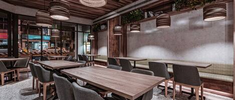 Un restaurante moderno con mesas y sillas de madera, iluminación colgante y vista a la calle.