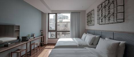 Una habitación de hotel moderna con dos camas, un ventanal grande, un televisor y un escritorio con taburetes.