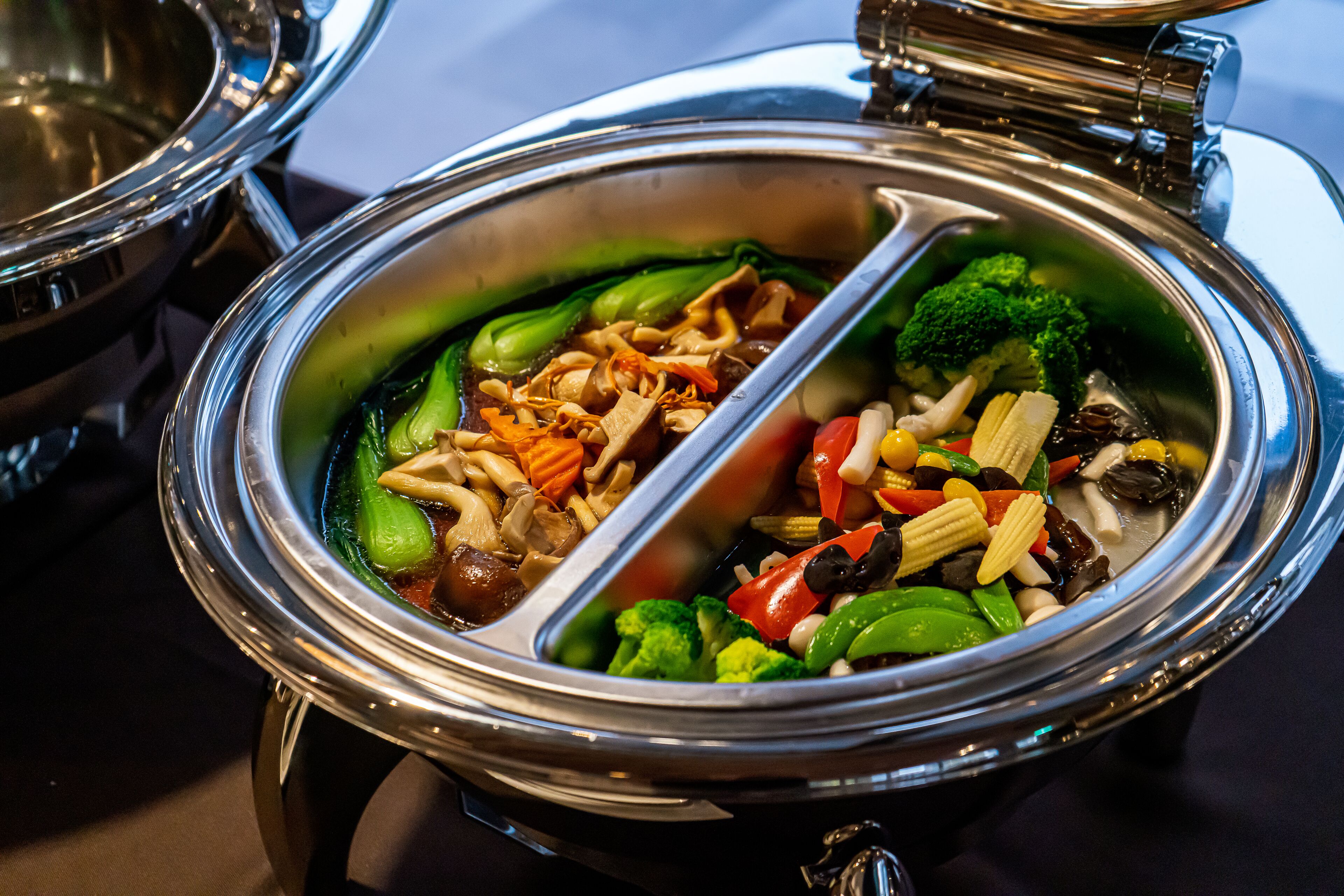 Un récipient alimentaire en acier inoxydable, doté de compartiments contenant différents légumes et champignons.