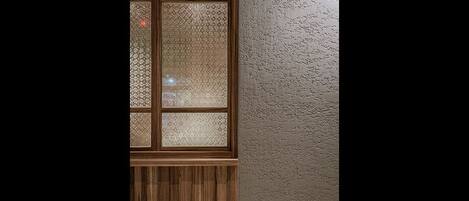 Een raam met houten kader en glas met structuur, geplaatst in een ruwe muur.