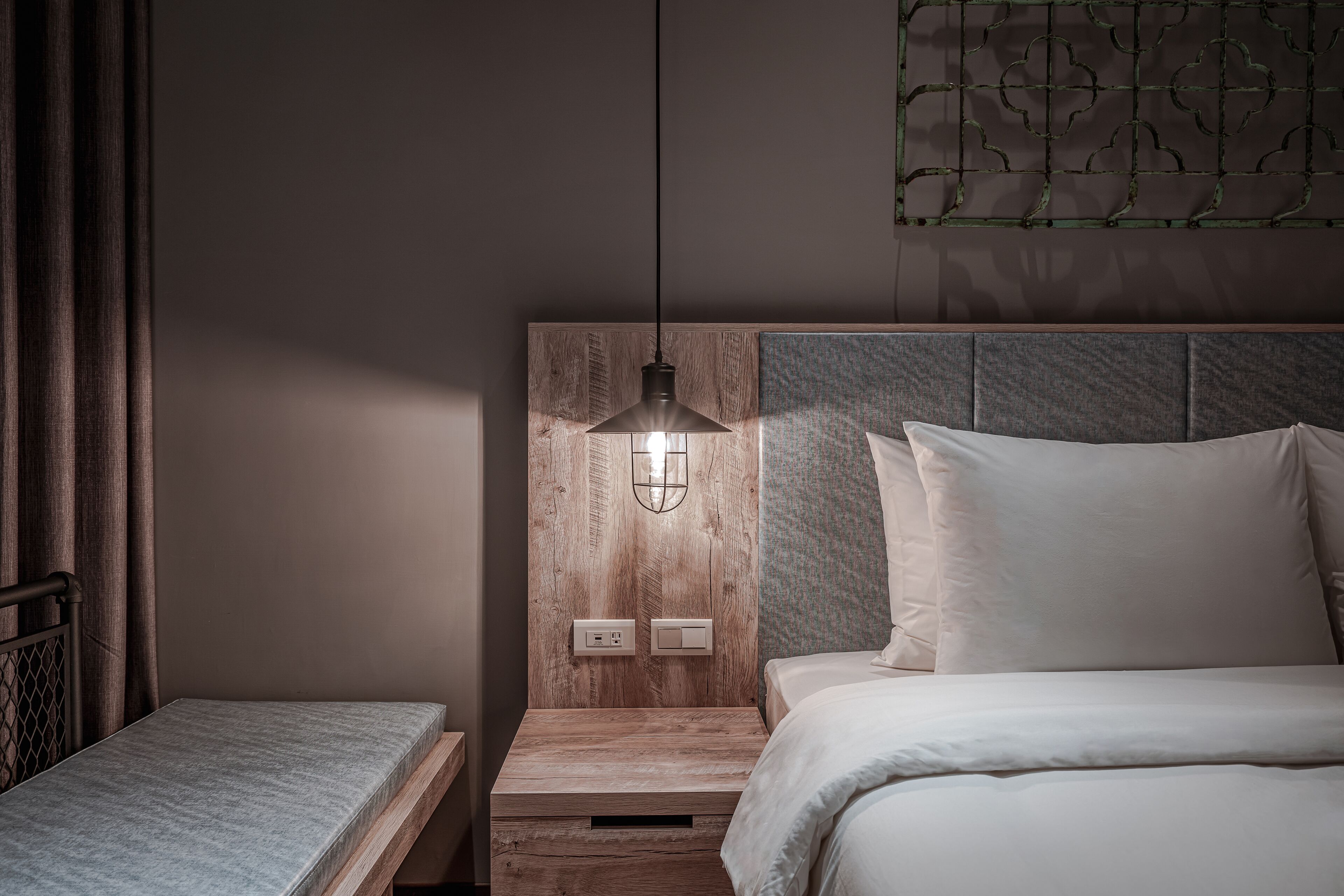 A bedroom with a bed, a bedside table, a nightstand, a hanging light fixture, and a wall-mounted light.