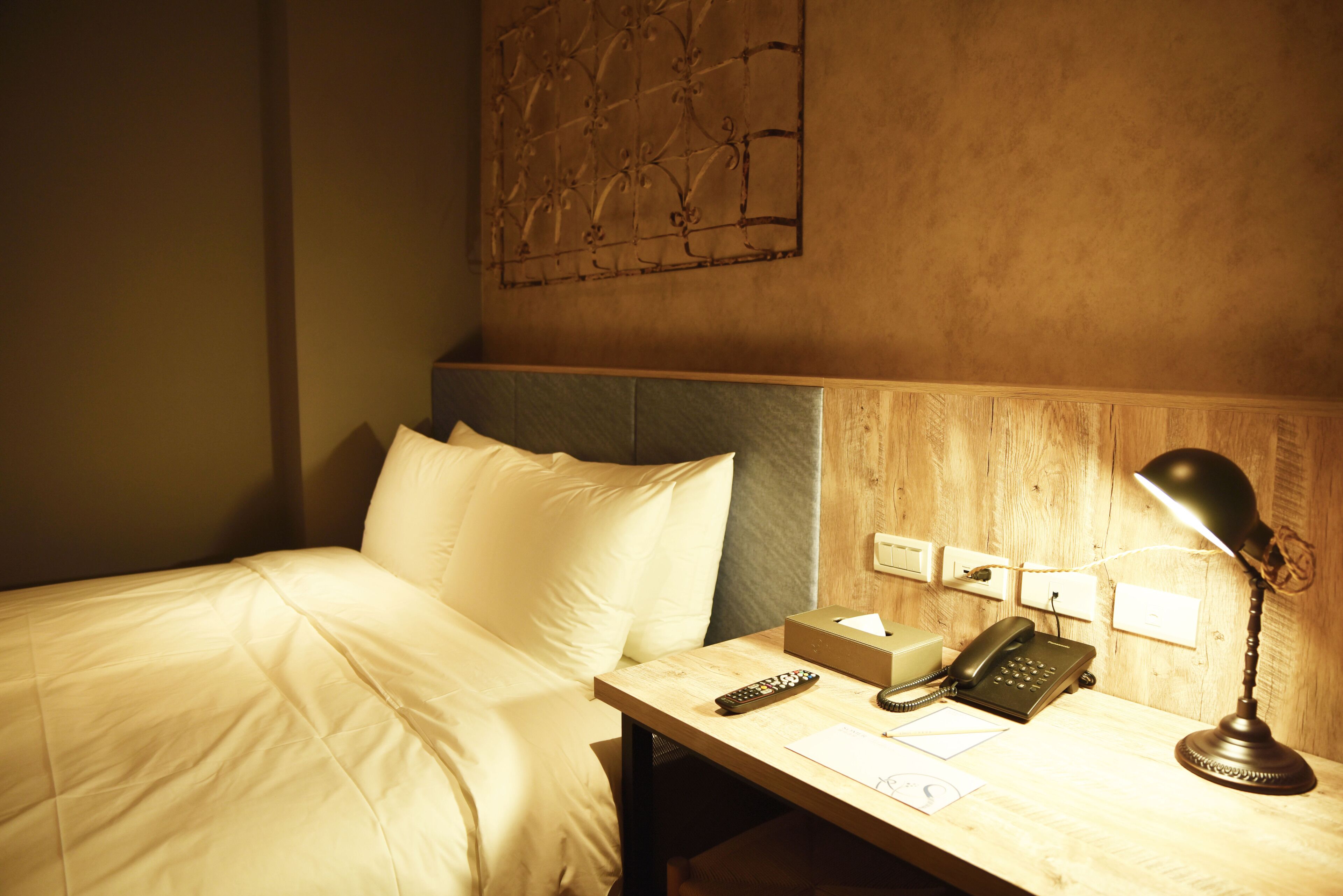Ein Hotelzimmer mit Bett, Nachttisch mit Lampe, Telefon und Wandbild.