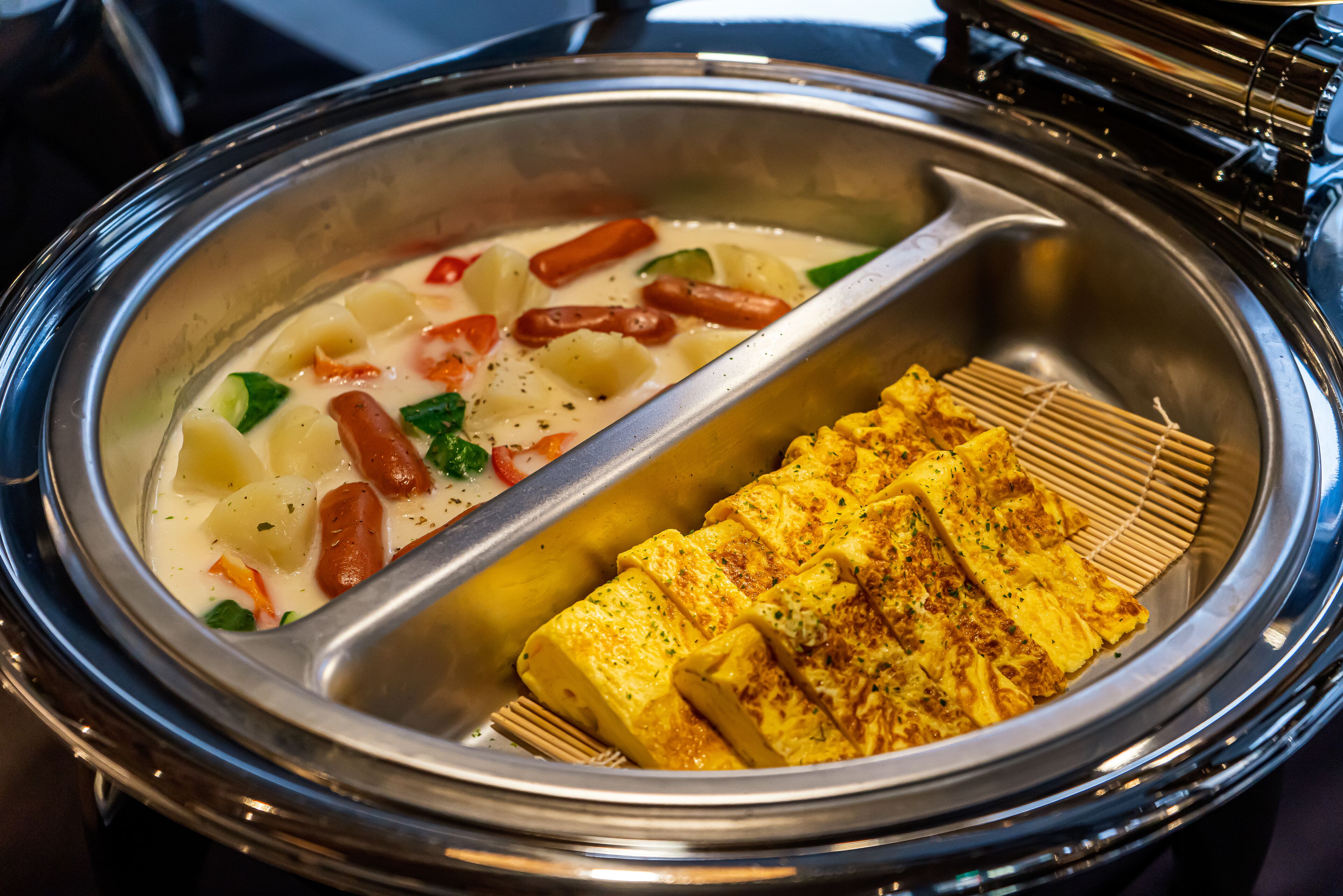 A buffet with a creamy soup containing vegetables and sausages, and a section with grilled fish.