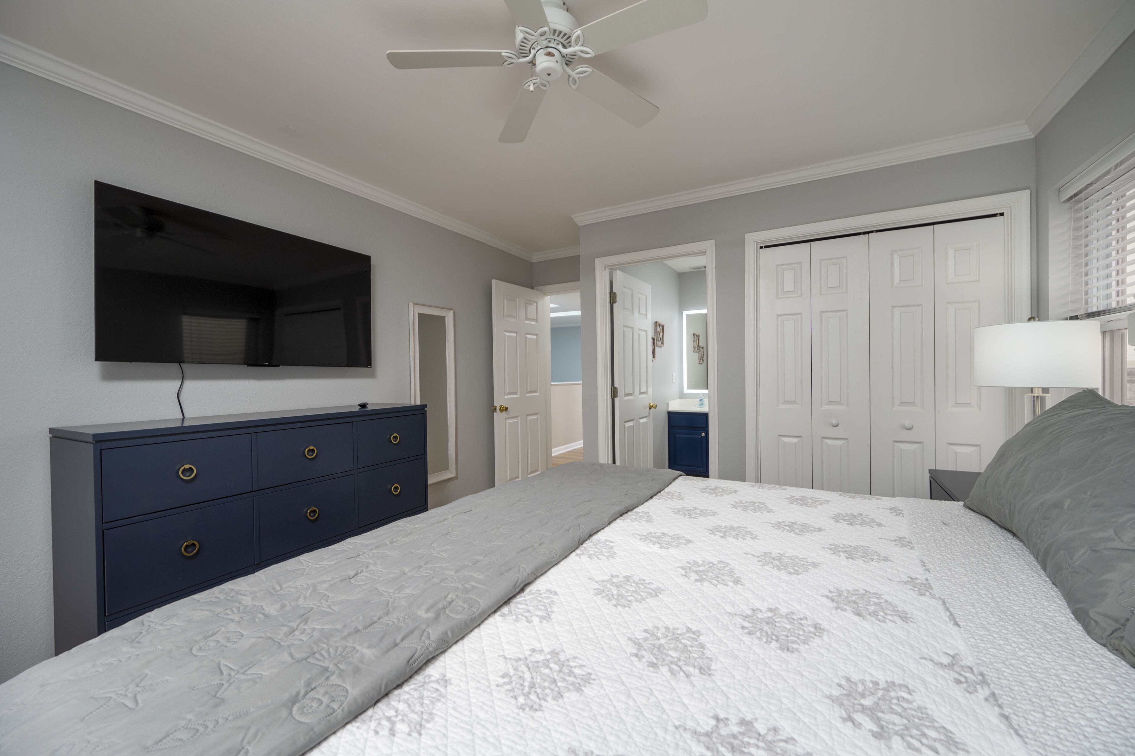 Ein Schlafzimmer mit Bett, Kommode, Deckenventilator und einem an der Wand montierten Fernseher.
