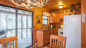 A cabin interior with wooden walls, a kitchen area, a dining table with chairs, and a large window overlooking a snowy landscape. - Secluded Cabin Outside of Nashville - The Lodge at Oak Haven Farm (White Bluff)