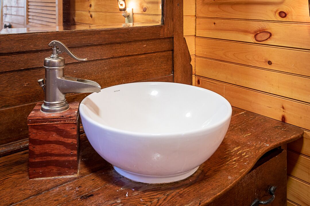 Un lavabo de cerámica blanca con un grifo antiguo sobre una encimera de madera en un ambiente rústico de cabaña.