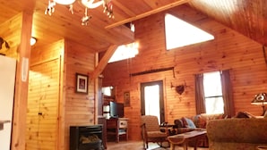 A log cabin interior with a wooden floor, a fireplace, a television, and a sofa. - Secluded Cabin Outside of Nashville - The Lodge at Oak Haven Farm (White Bluff)