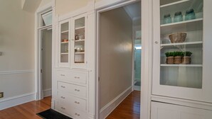 Una habitación amplia con piso de madera, un armario empotrado blanco con varios cajones y puertas de vidrio, y un ventanal pequeño.