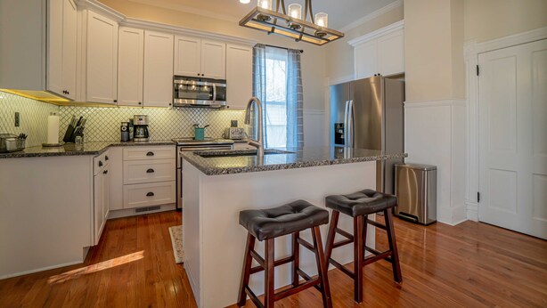 Una cocina moderna con armarios blancos, electrodomésticos de acero inoxidable y una isla central con taburetes.