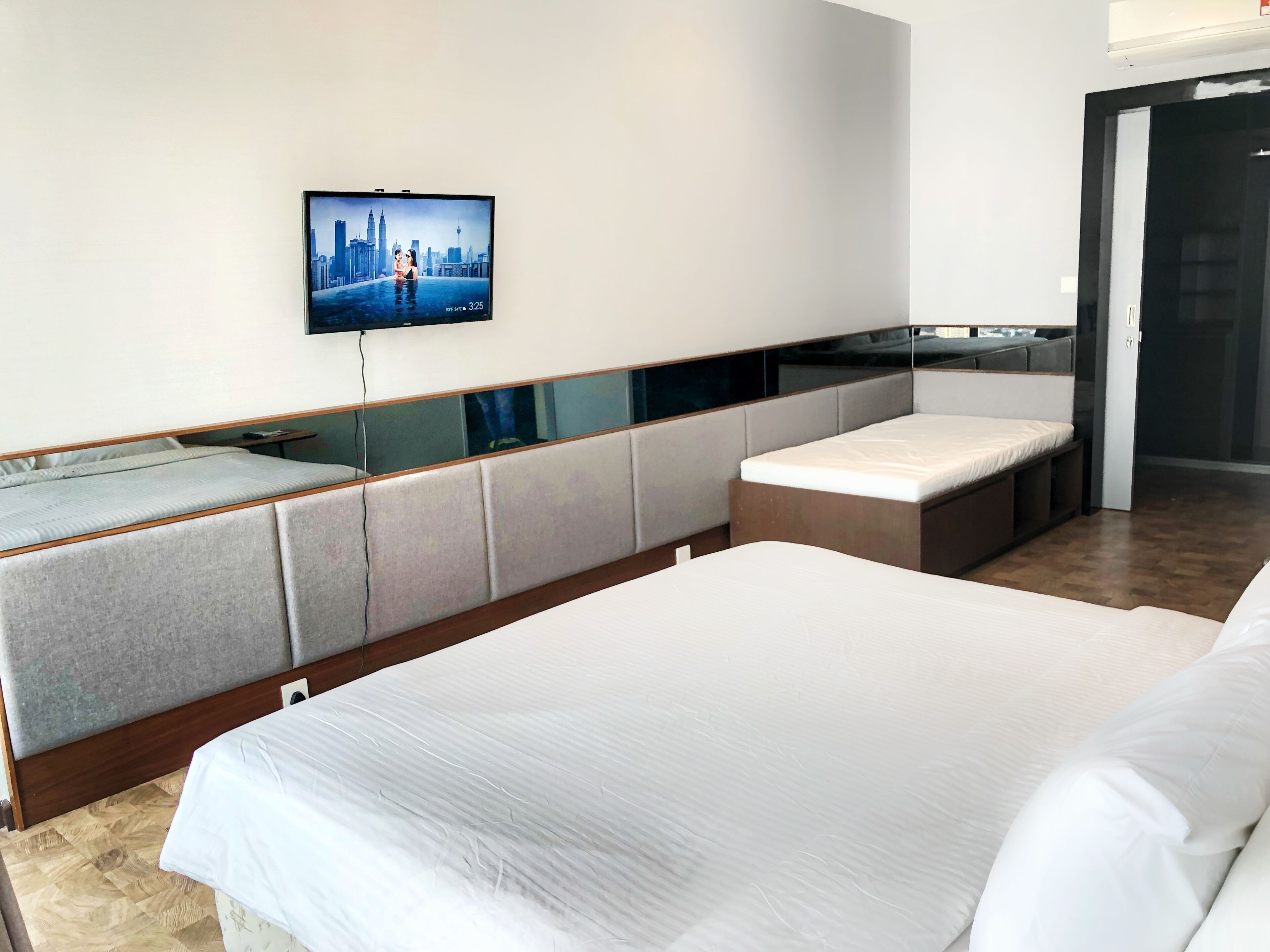 A modern hotel room with a large bed, a seating area with a TV displaying a cityscape, and a door leading to another room.