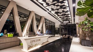 A modern reception area with a geometric ceiling design, a reception desk labeled "EXPRESSIONZ," and a large potted plant. - Expressionz Suites KLCC by Like Home (Kuala Lumpur)