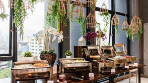 A buffet setup with various food stations, hanging plants, and a city view through large windows. - Expressionz Suites KLCC by Like Home (Kuala Lumpur)