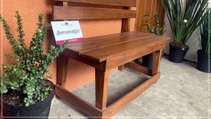 Una panchina di legno con un cartello che recita 'Bienvenido@S!' di fronte a una parete arancione strutturata.