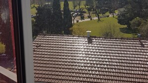 Vista des d'una finestra sobre una zona residencial amb terrasses de teules, un aiguabarreig i un paisatge verd.
