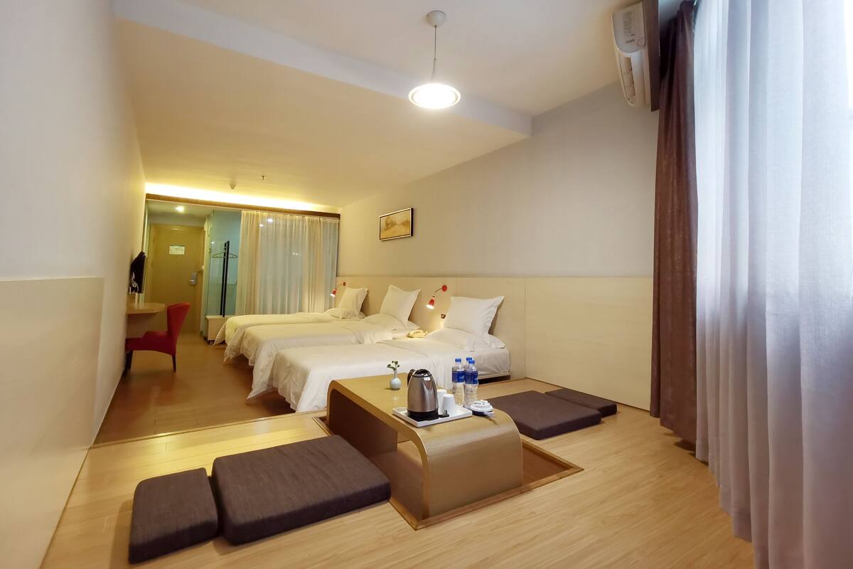 Une chambre d’hôtel avec deux lits, un bureau avec une bouilloire et des bouteilles d’eau, un canapé et un espace douche.