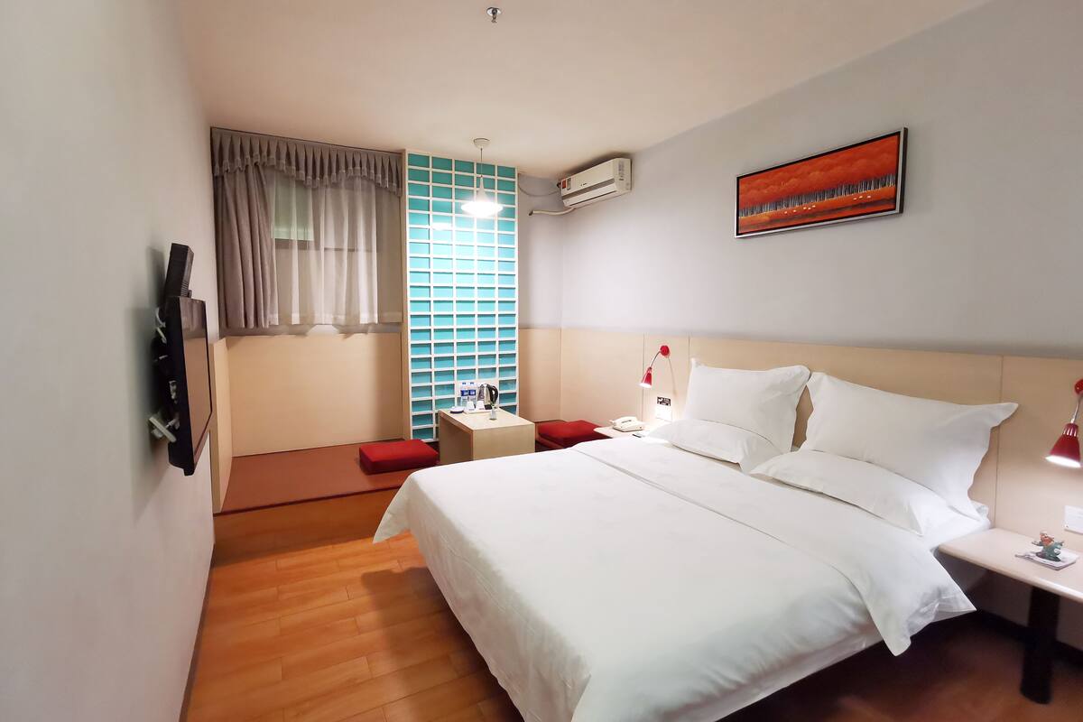 Une chambre d’hôtel équipée d’un lit, d’une table de chevet, d’une lampe, d’un climatiseur et d’une fenêtre avec des rideaux.