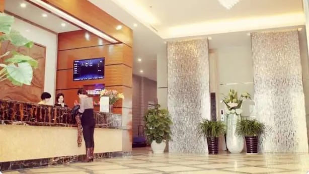 Een hotel receptie met een marmeren balie, een televisiescherm en potplanten.