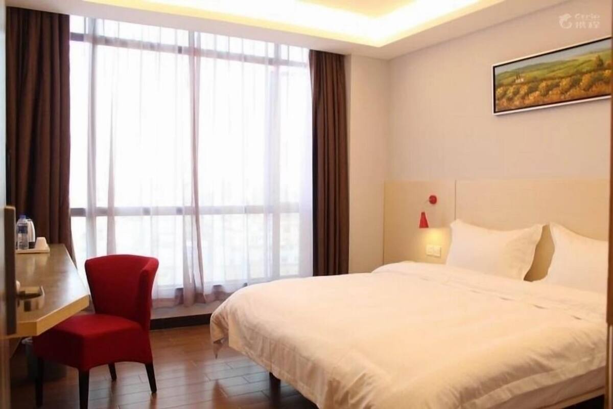 Une chambre d’hôtel avec un grand lit, un bureau avec une chaise et une fenêtre avec des rideaux.