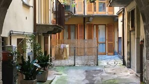 Um beco estreito com edifícios de ambos os lados, com varandas adornadas com plantas e venezianas de madeira.
