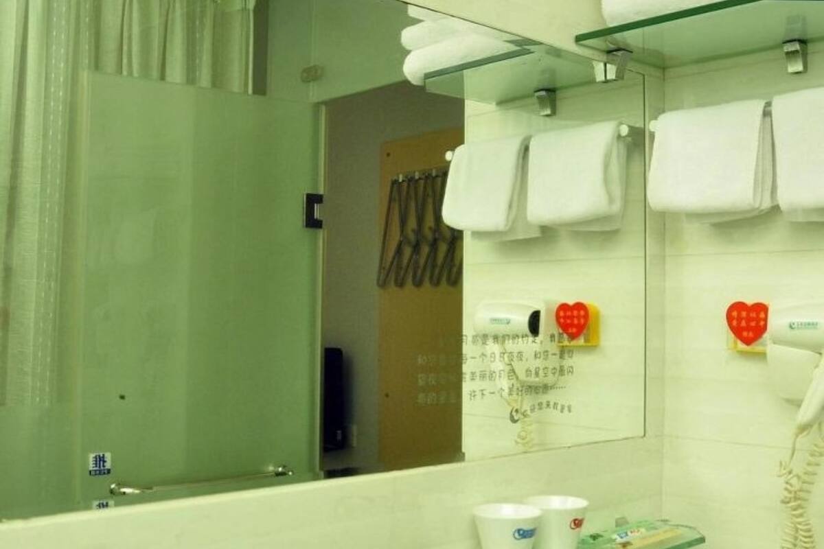 Un baño con un espejo grande, un estante de vidrio con artículos de aseo y un secador de pelo en la pared.