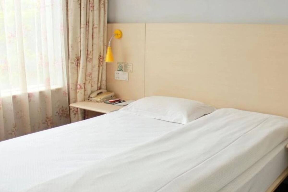 Una cama bien hecha con sábanas blancas en una habitación con cabecera de madera, una mesita de noche con lámpara y teléfono.