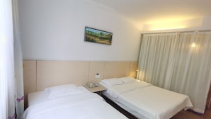 Habitación de hotel con dos camas individuales, una mesita de noche con un teléfono y una revista, un cuadro en la pared y una ventana con cortinas.