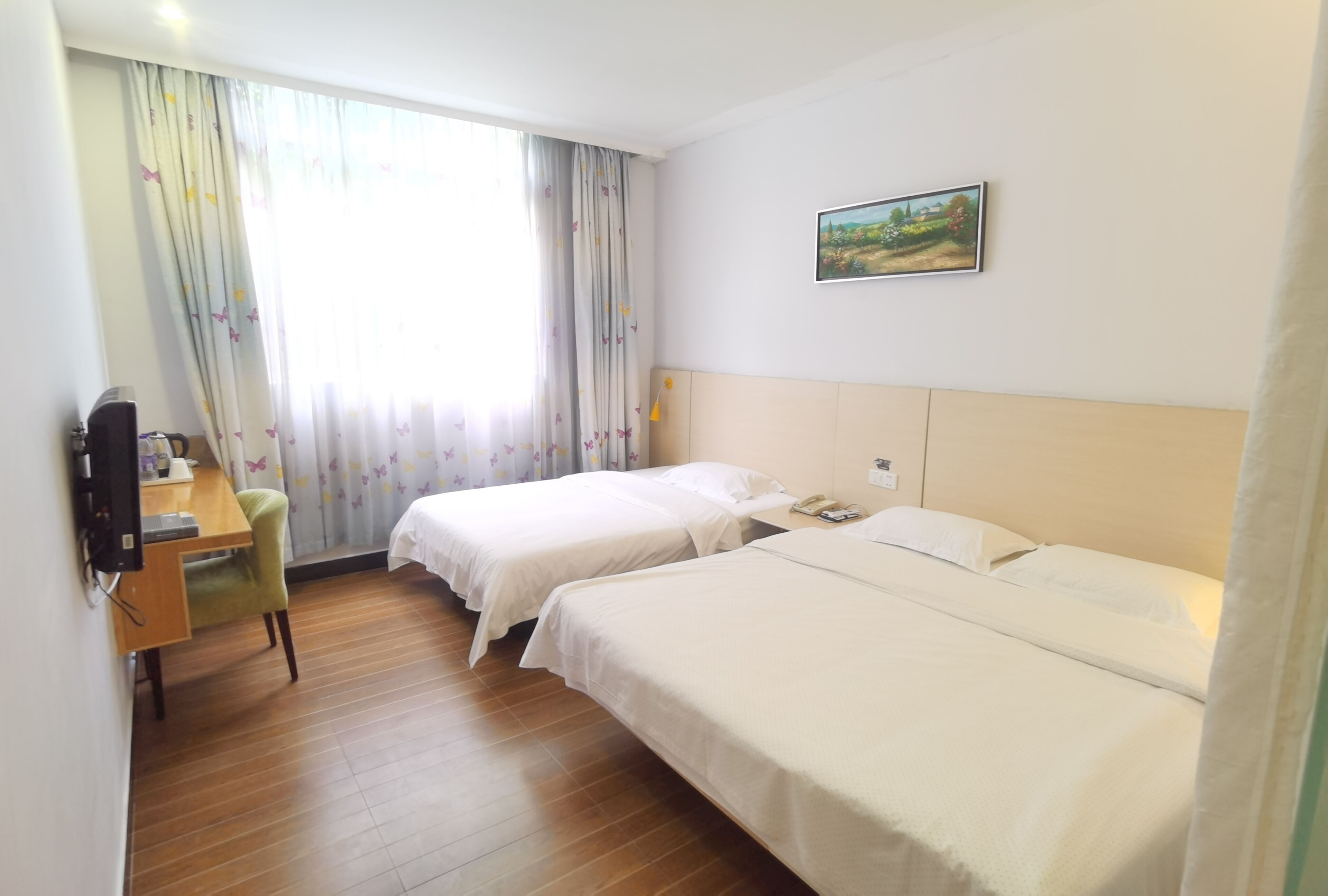 A hotel room with two beds, a desk with a chair, a television, and a painting on the wall.