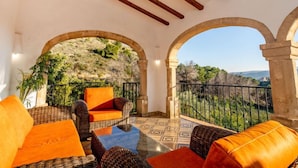 Une terrasse dotée de meubles en osier et de coussins orange, d’arches en pierre et offrant une vue sur un paysage montagneux.
