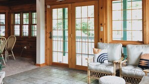 A spacious living room with wooden beams, a large window, and a sunburst decoration above the door.