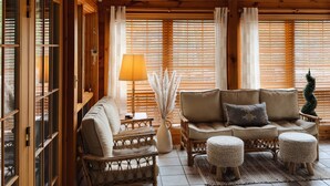 A cozy room with wooden beams, a star-shaped hanging light, a sofa set, and a window with blinds.