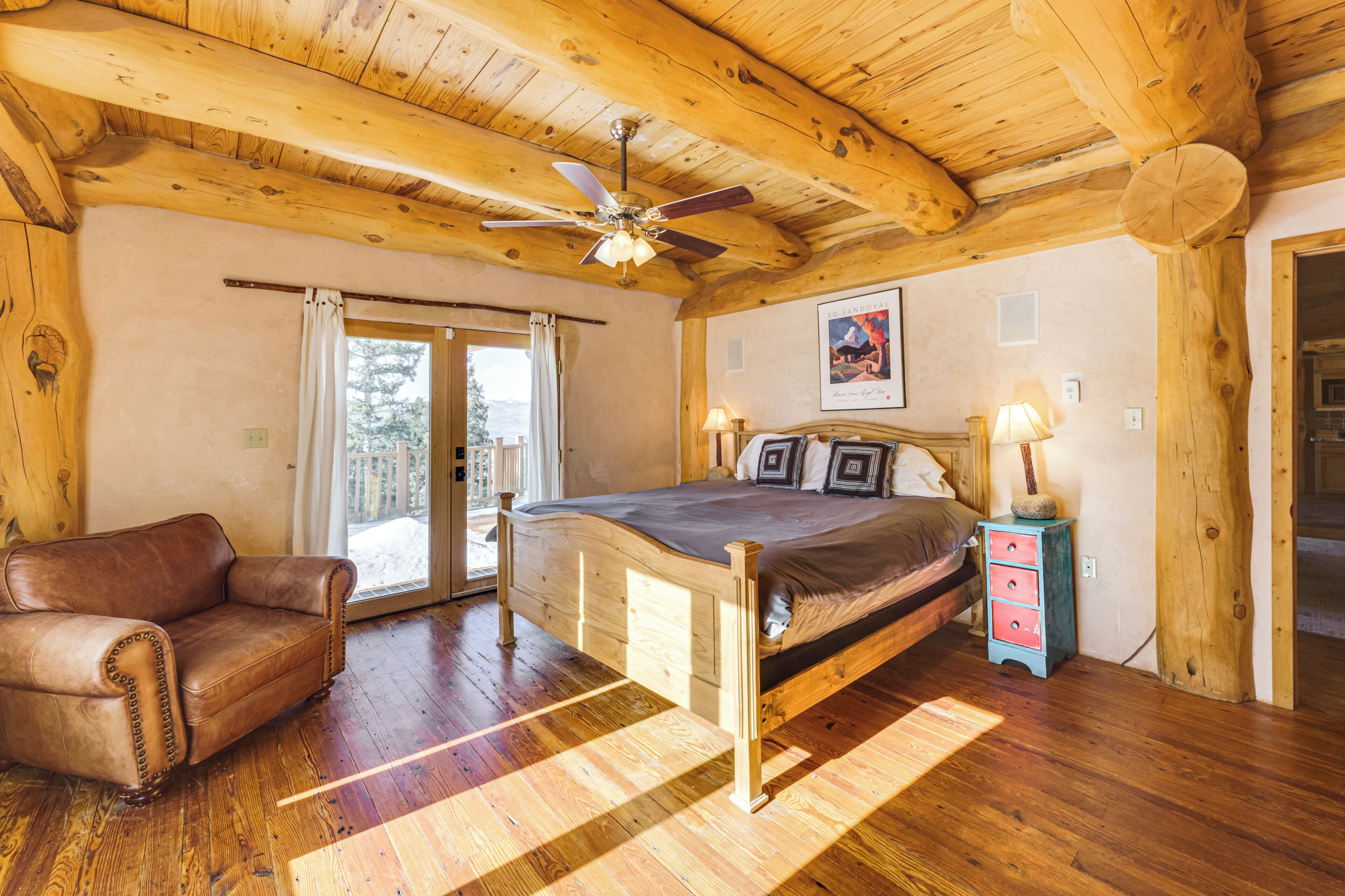 A wooden cabin bedroom with a bed, a chair, a ceiling fan, and a window.