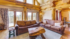 L’intérieur chaleureux d’un chalet en rondins est agrémenté de deux canapés en cuir, d’une table basse en bois et de grandes fenêtres offrant une vue sur l’extérieur.