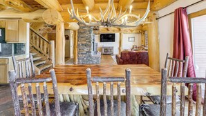 Un coin repas rustique avec une grande table et des chaises en bois, une cheminée en pierre et un téléviseur en arrière-plan.
