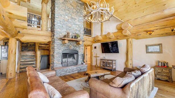L’intérieur d’une cabane en rondins, avec une cheminée en pierre, des canapés en cuir, un plancher en bois et un téléviseur fixé au mur.