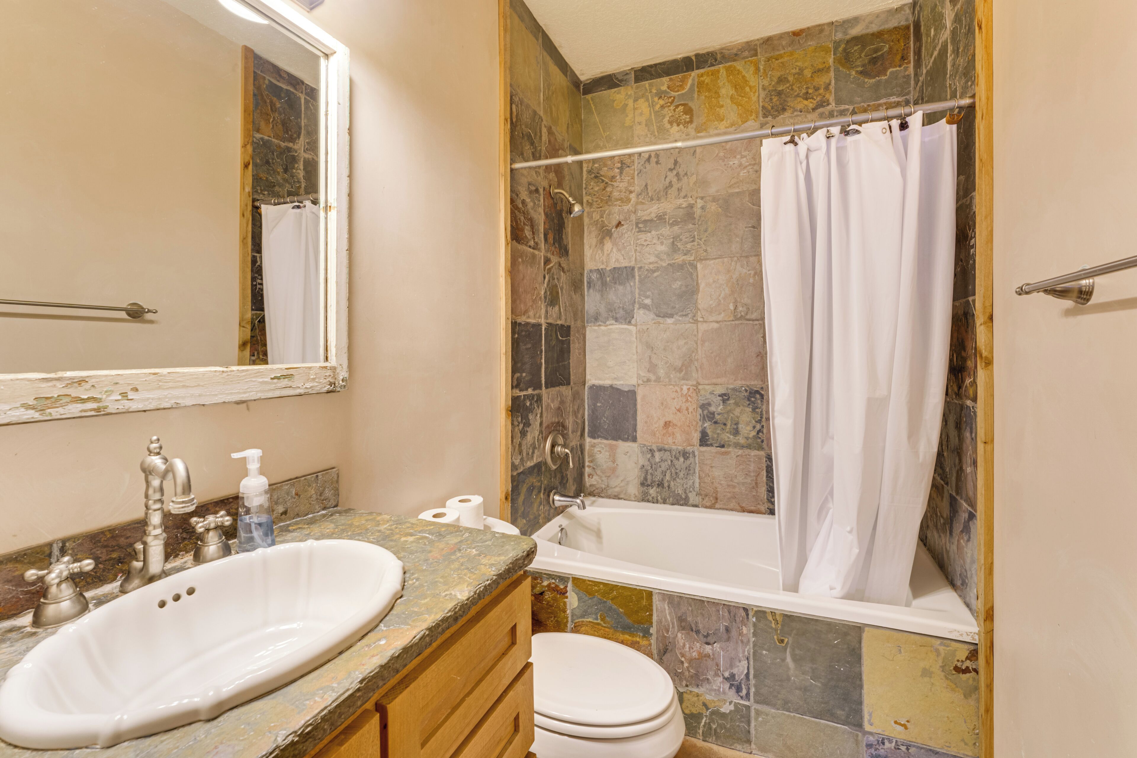 Un baño con ducha de azulejos de piedra, una bañera blanca, un lavamanos con encimera de mármol y un inodoro.