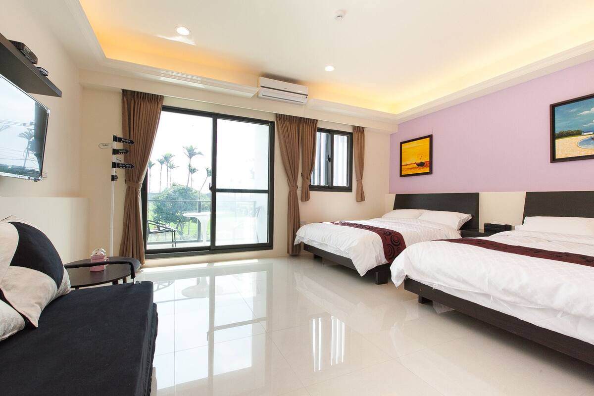 A hotel room with two beds, a desk, a chair, a TV, and a large window with curtains.
