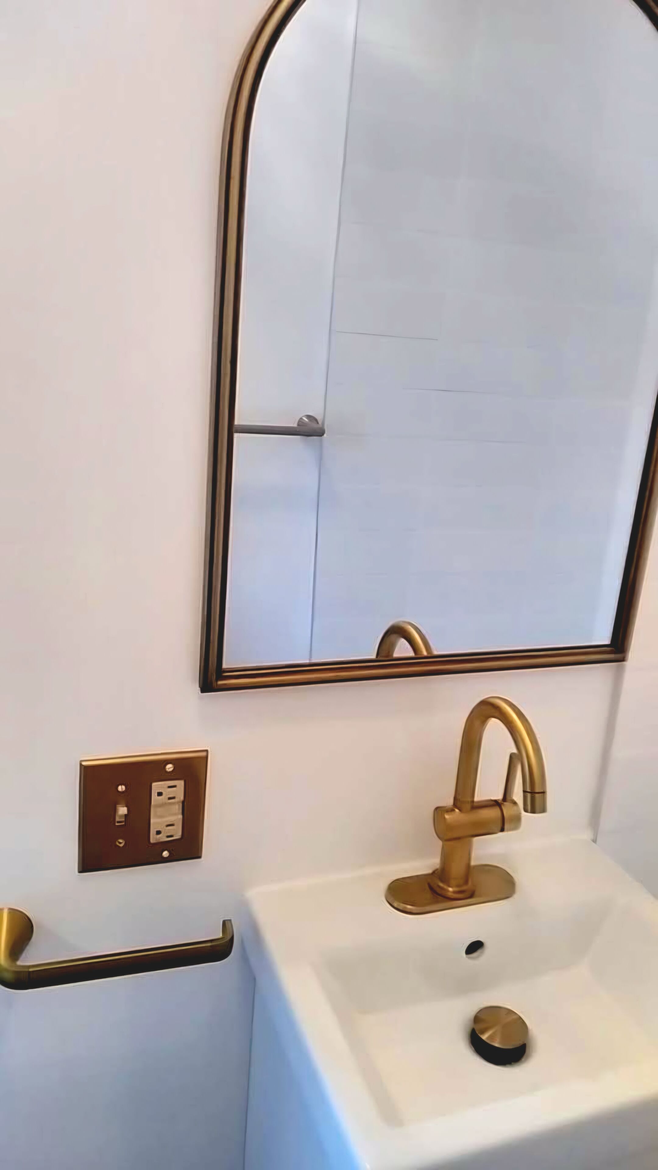 Ein Badezimmer mit einem weißen Waschbecken, einem goldenen Wasserhahn und einem Spiegel mit goldener Rahmung.