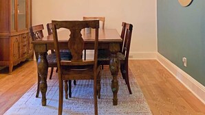Ein Esszimmer mit Holztisch und -stühlen, einer Chandelierleuchtre, einer Holzkommode und einem wandmontierten Spiegel.