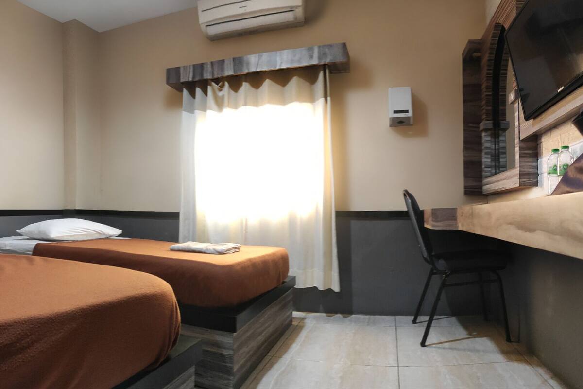 A hotel room with two beds, a desk, a chair, and a window with curtains.