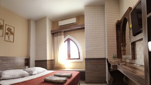 A hotel room with a bed, a wooden desk, an air conditioning unit, and a window with curtains. - Hotel Syariah Larismanis (Semarang)