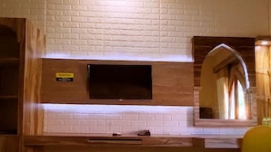 A hotel room with two beds, a flat-screen TV mounted on a brick wall, a wooden vanity with a mirror, and a window with curtains. - Hotel Syariah Larismanis (Semarang)