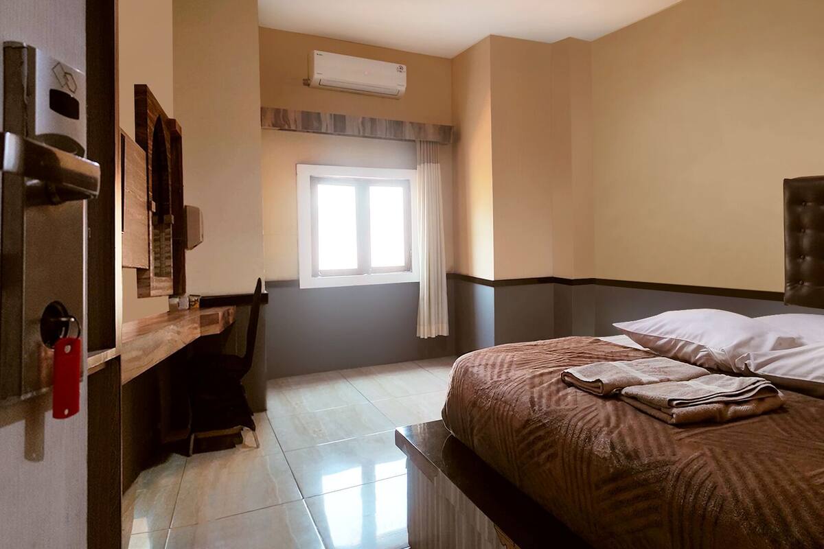 A hotel room with a bed, a desk, a chair, and a window with curtains.