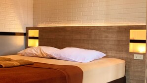 A hotel room with a bed, white pillows, a brown blanket, and wall-mounted lights.