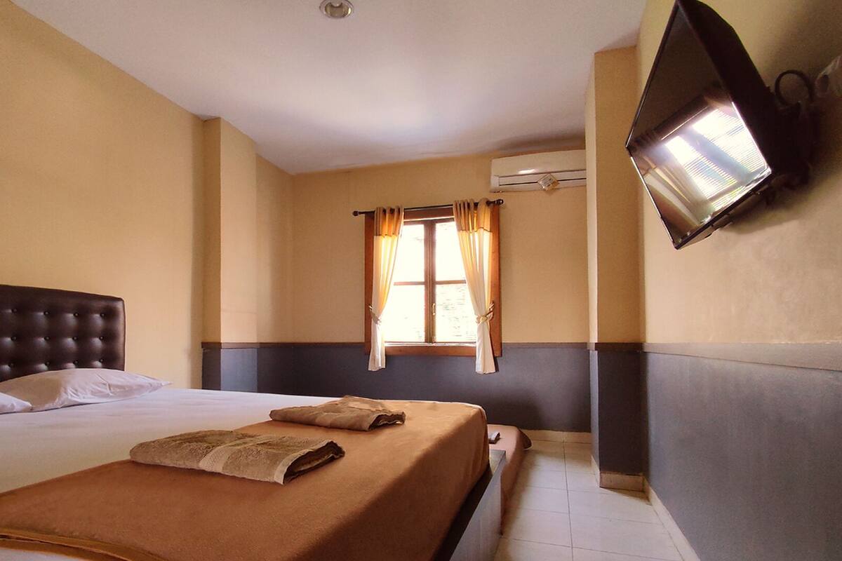 A hotel room with a large bed, a flat-screen TV mounted on the wall, and an air conditioning unit.