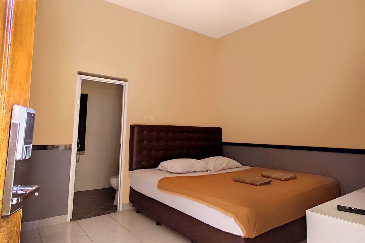 A bedroom with a bed, a bedside table, and a door leading to a bathroom.