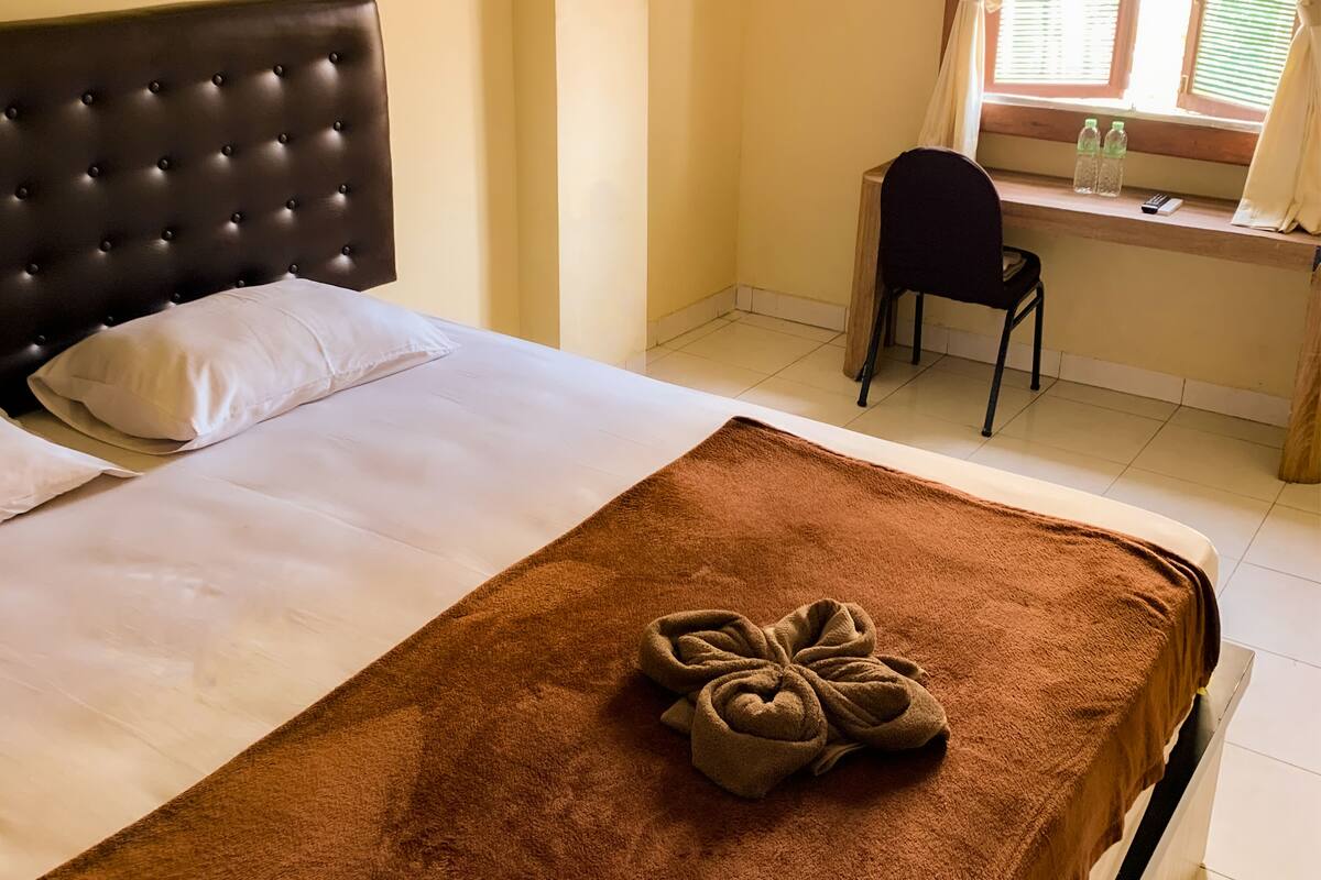 A neatly made bed with a brown towel, a black upholstered headboard, and a white pillow.