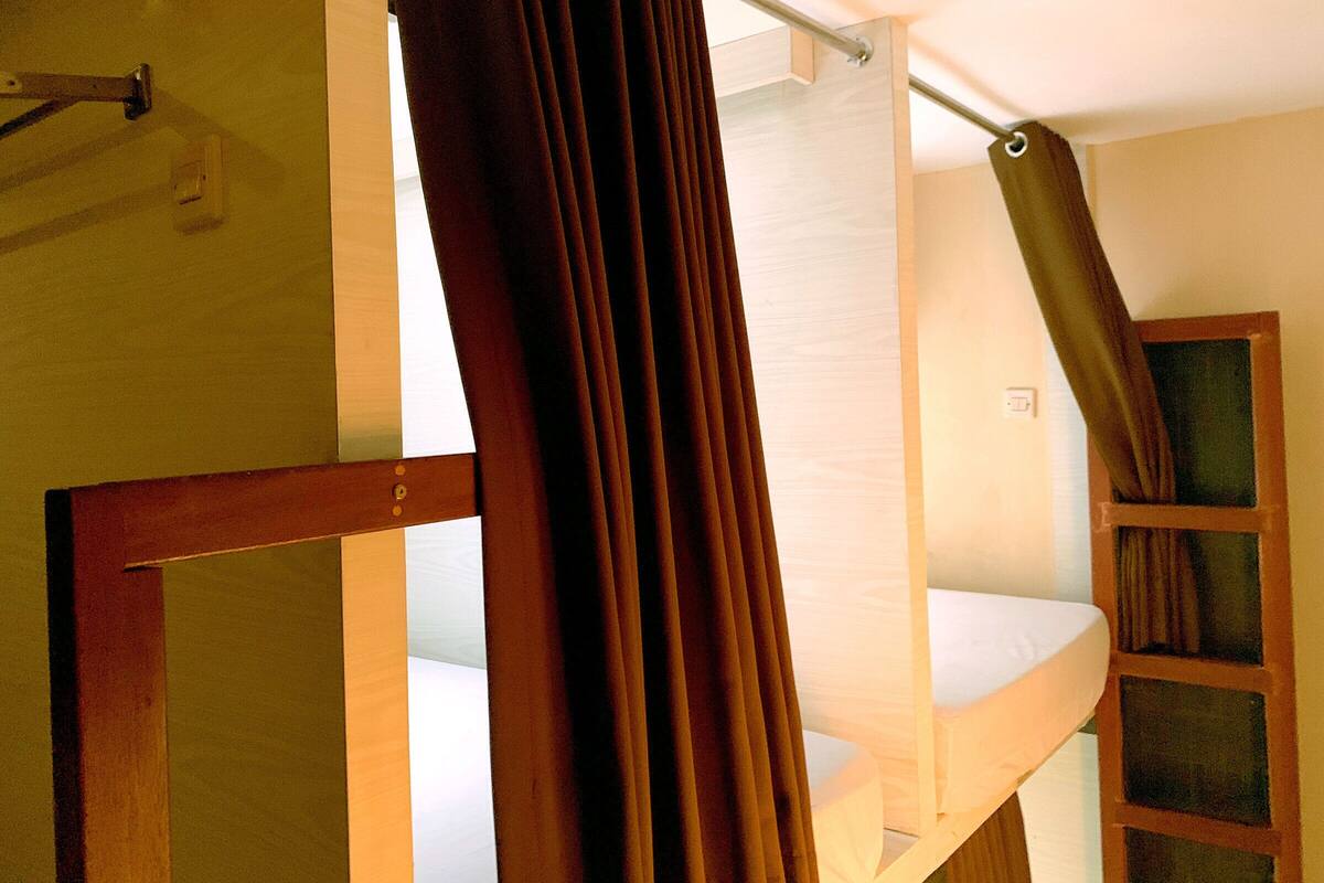 A bunk bed with a curtain, a wooden frame, and a window with a curtain.