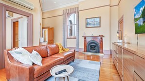 A living room with a leather sofa, a fireplace, a television, and a large window. - Clocktower Suites (Echuca)