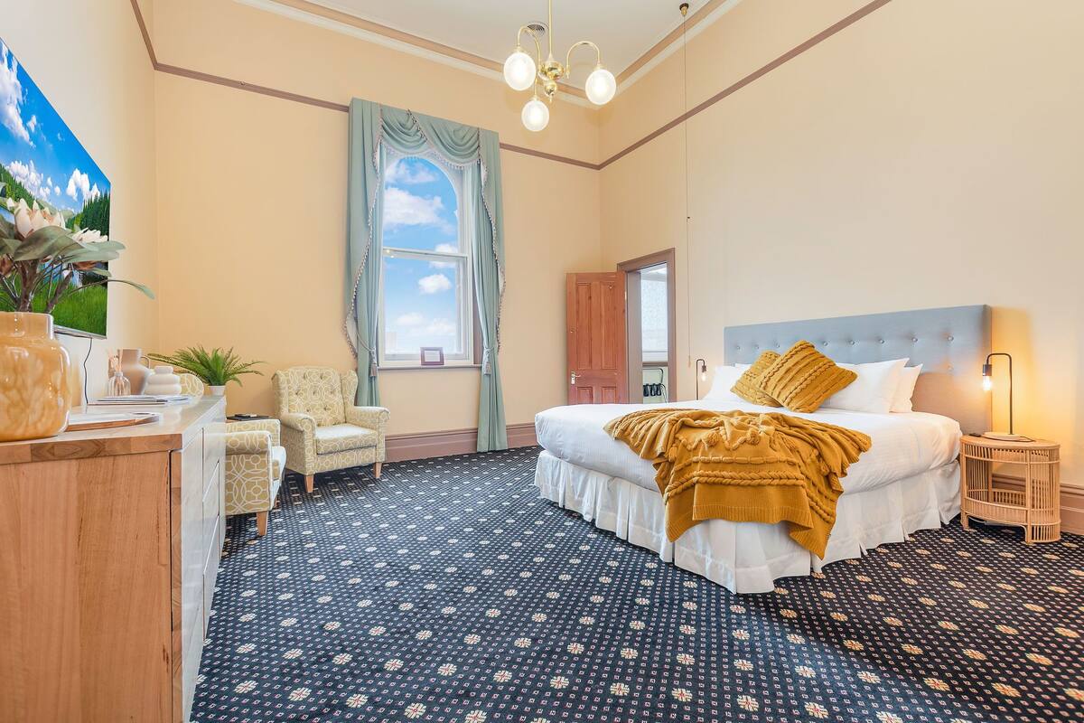 A bedroom with a bed, a chair, a desk, and a large window with curtains.