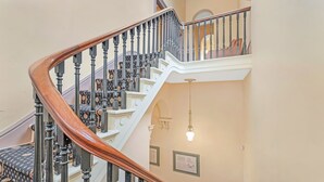 A grand staircase with ornate black balusters and a wooden handrail, leading to a second-floor landing with a view of the interior. - Clocktower Suites (Echuca)